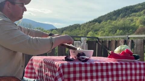 Man Preparing Vegetables at Rustic Outdoor Table with Scenic View Stock Footage 333523422