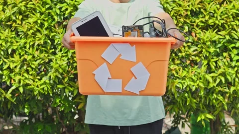 Man presenting e-waste sorting box against lush green foliage background Stock Footage 340578462