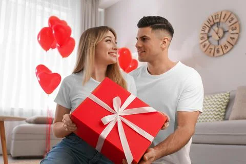 Man presenting gift to his girlfriend in room decorated with heart shaped bal Stock Photos