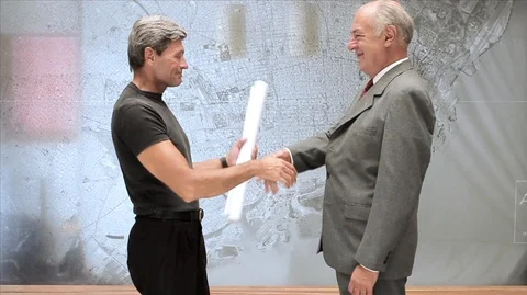 Man presenting rolled documents/building plans to a businessman and then shaking Vídeos de archivo 88407129