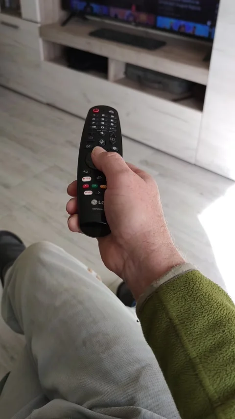 A man presses the buttons on the TV remote control while sitting in a chair Stock Footage 164111207