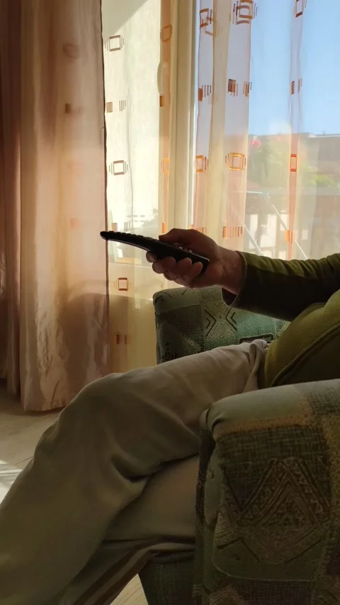 A man presses the buttons on the TV remote control while Stock Footage 164550107