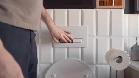 A man presses the flush button in a modern toilet. Daily morning toilet visits Stock Footage 267091995