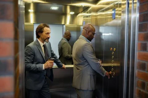 Man pressing button in elevator while standing near colleague Stockfoto's