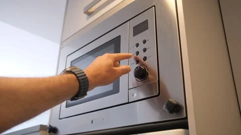 Man pressing control buttons on a built-in microwave oven in a modern kitchen Stock Footage 325845177