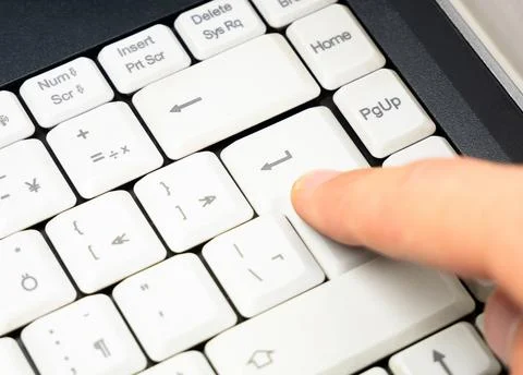 Man pressing the enter key on a simple plain white laptop keyboard, finger Stock Photos