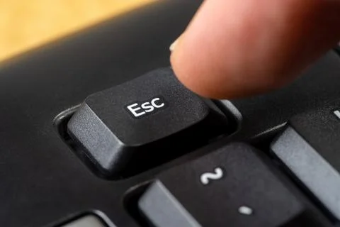 Man pressing the escape key on a simple black office keyboard, finger pushing Stock Photos