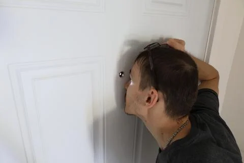 Man pressing hand on door while looking through peephole security concept Stockfoto's