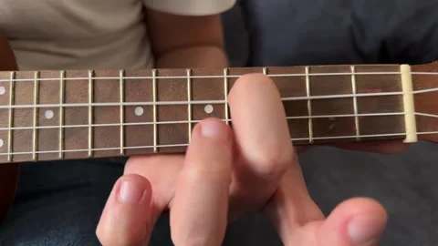 Man pressing strings on ukulele fretboard close up at home, playing chord, music Stock Footage 337104419