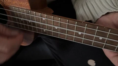 Man pressing strings on ukulele fretboard close up at home, playing chord, music Stock Footage 337105379