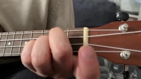 Man pressing strings on ukulele fretboard close up at home, playing chord, music Stock Footage 337105380
