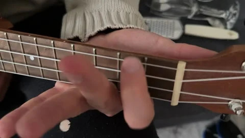 Man pressing strings on ukulele fretboard close up at home, playing chord, music Stock Footage 337105389