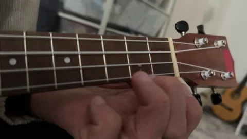 Man pressing strings on ukulele fretboard close up at home, playing chord, music Stock Footage 337105390
