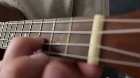 Man pressing strings on ukulele fretboard close up at home, playing chord, music Stock Footage 337105399