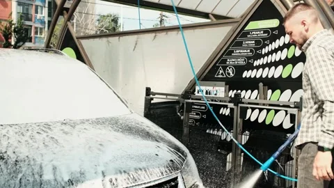 Man pressure washes black auto Volkswagen TOURAN covered in thick white foam at Stock Footage 312677564