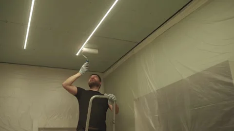 A man primes a drywall ceiling with a roller Stock Footage 323116346