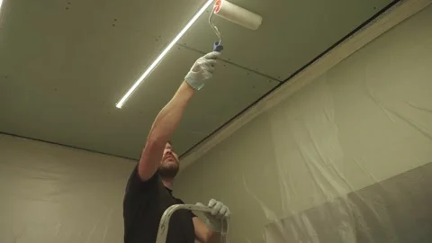 A man primes a drywall ceiling with a roller Stock Footage 323116363