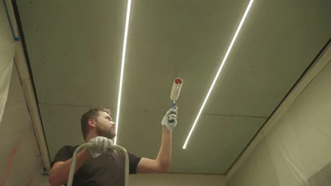 A man primes a drywall ceiling with a roller Stock Footage 323116604