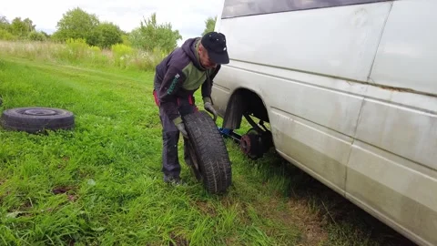 A man is in the process of changing a tire on a van, positioned in a grassy patc Video stock 347164542