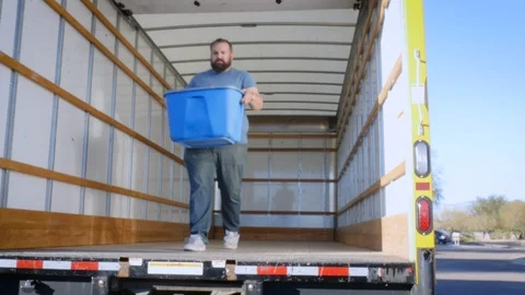 Man in the Process of Relocation Unloads a Blue Plastic Bin from a Moving Truck Stock Footage 89297476