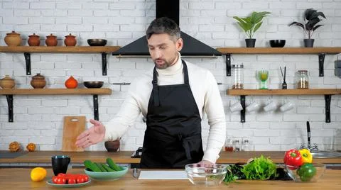 Man professional chef in home kitchen tells shows ingredients for cooking salad Stock Photos