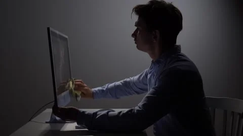 Man in profile sitting at a desk, carefully cleaning a dusty computer screen Stock Footage 342672870