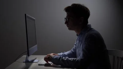 Man in profile wearing glasses working intently on a computer in a dimly lit Stock Footage 342672753