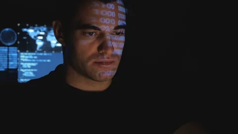 Man programmer hacker working on a computer while blue code characters reflect Vidéo 102927667