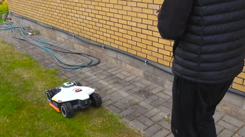 Man Programming Automatic Robotic Lawn Mower with Smartphone Stock Footage 337496070
