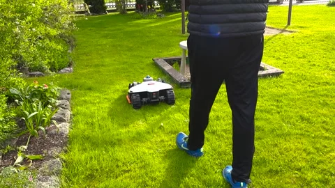 Man Programming an Electric Robotic Lawn Mower in the Garden 動画素材 336651942