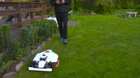 Man Programming Robotic Lawn Mower with a Smartphone in the Garden Stockbeeldmateriaal 336651954