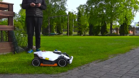 Man Programming a Smart Robotic Lawn Mower with a Smartphone Stock Footage 337904927