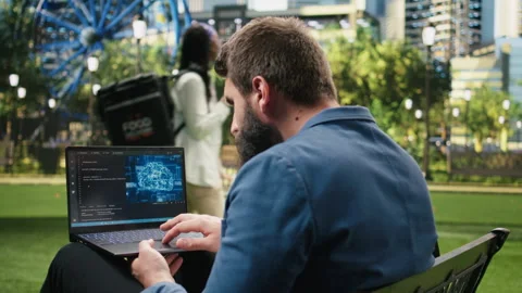 Man programs AI interface and source code on laptop in urban park Stock Footage 348401677