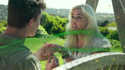 Man proposing wedding, sliding ring onto her finger on bench, green particles Stock Footage 333192724