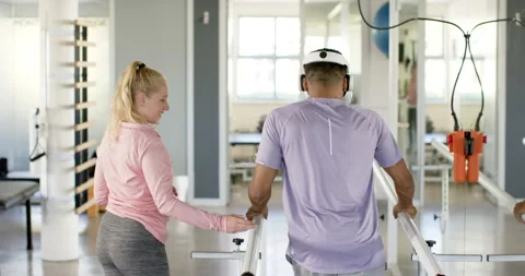 Man in prosthetic leg walking using VR headset with therapist on parallel bars Stock Footage 300148193