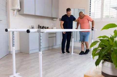 Man with prosthetic leg walking using parallel bars with therapist in clinic Stock Photos