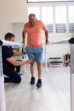 Man with prosthetic leg walking using parallel bars with therapist assisting Stock-Fotos