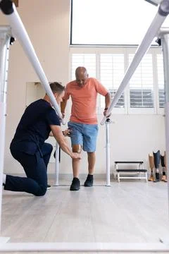 Man with prosthetic leg walking using parallel bars with therapist assisting Stock Photos