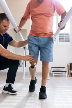 Man with prosthetic leg walking using parallel bars with therapist assisting Stock-Fotos