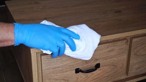 A man in protective blue gloves washes the furniture on the nightstand with a Stock Footage 126927503