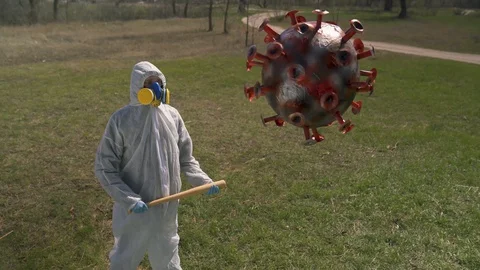 Man in protective clothes holds a baseball bat and walks to a coronavirus pinata Stock Footage