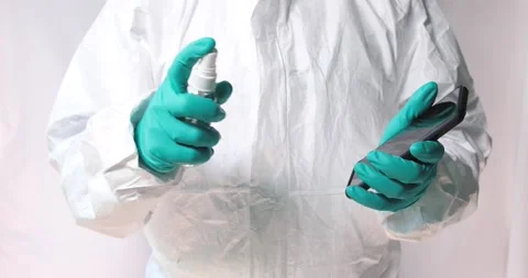 Man with protective clothes using alcohol spray on the smartphone Stock Footage 134075233