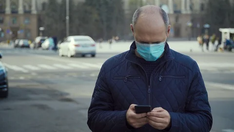 Man in protective face mask typing message on smart phone and bicyclist with Stock Footage 127560428
