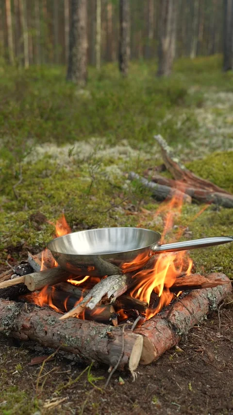 A man in protective gloves is placing a frying pan over a campfire to heat it up Stockbeeldmateriaal 310319090