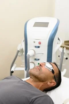 Man in protective goggles lying on bed in treatment room Stock Photos