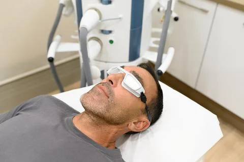 Man with protective goggles lying on bed in treatment room Stock Photos