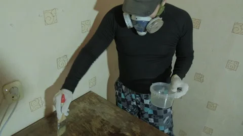 Man in a protective mask and construction gloves varnishes an old wooden table Stock Footage 145322965
