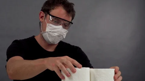 The man in protective mask and glasses to build a pyramid out of toilet paper Stock Footage 129051685