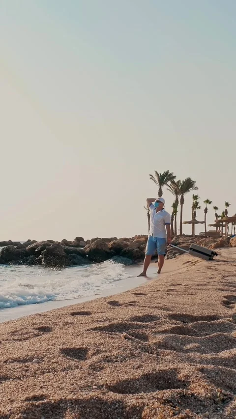 Man in protective mask and summer clothes, enjoys warm sunbeams, by the sea, Stock Footage 316468868