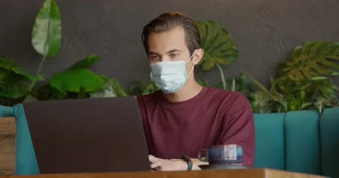 Man in protective mask having a cup of coffee in cozy cafe during COVID.Young Stock Footage 164714146